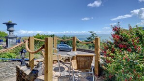 A patio with a wicker chair, a stone table, and a view of the ocean. - 2 Bed in Lynton (oc-cslewt) (Lynmouth)