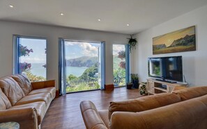 A spacious living room with a large TV, leather sofas, and a scenic view through the windows.