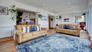 A spacious living room with two leather sofas, a large blue patterned rug, and hanging plants. - 2 Bed in Lynton (oc-cslewt) (Lynmouth)