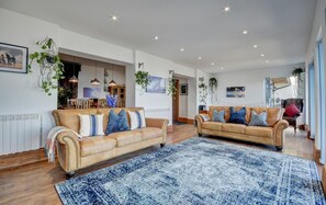 A spacious living room with two leather sofas, a large blue patterned rug, and hanging plants.