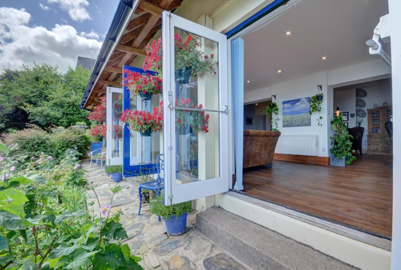Une maison moderne avec un chemin en pierre, des jardinières suspendues et un intérieur en bois.