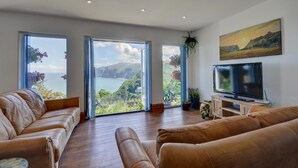 A spacious living room with a large TV, leather sofas, and a scenic view through the windows. - 2 Bed in Lynton (oc-cslewt) (Lynmouth)