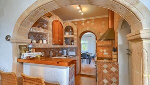A kitchen with an archway, a bar area with wicker chairs, and a dining area in the background.