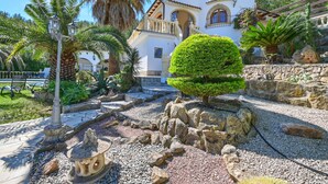 A Mediterranean-style villa with a well-maintained garden, stone pathway, and a small fountain.