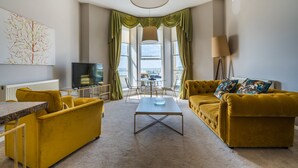 Un salon avec un canapé, une table basse, un téléviseur et une fenêtre avec des rideaux.
