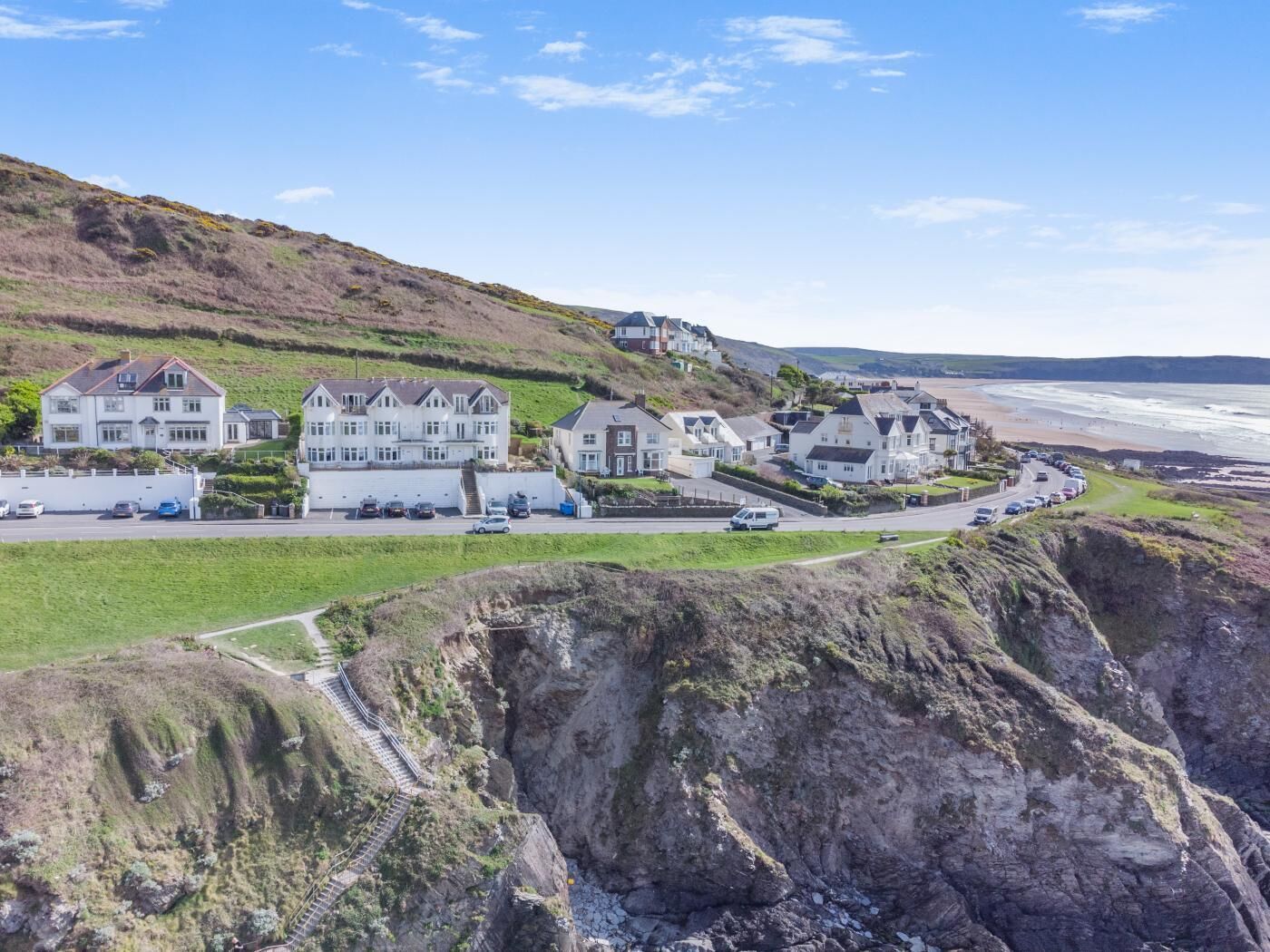 Une zone résidentielle côtière avec des maisons, une route et une falaise surplombant la mer.