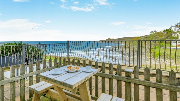 A wooden deck with a table and chairs overlooking a beach with a fence. - 1 Bed in Woolacombe (oc-waves) (Woolacombe)