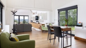 Un salon moderne avec un canapé vert, une table à manger avec des chaises et un coin cuisine visible à travers une porte ouverte.