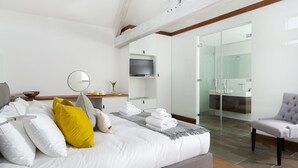 Une chambre d’hôtel moderne dotée d’un grand lit, d’une télévision, d’une douche en verre et d’un coin salon.