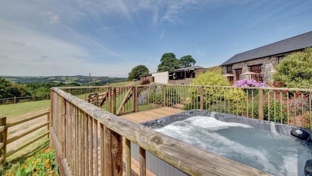 Een houten terras met een jacuzzi, omringd door een houten schutting en bloeiende planten.