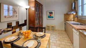 Un coin repas avec une table en bois dressée pour quatre personnes, un panier de fruits, et une cuisine équipée d’un évier et de placards.
