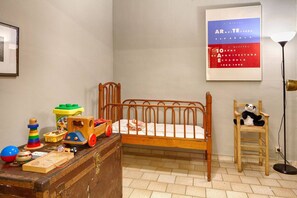 A child's bedroom with a wooden bed, a small wooden chair, a panda plush toy, a suitcase, and a poster on the wall.