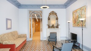 Un salon avec un sol à motifs, un canapé, un fauteuil, une cheminée, un téléviseur et un grand tableau.