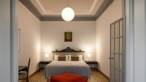 Une chambre d’hôtel avec un lit, un pouf rouge, une table de chevet, une lampe et un tableau encadré au mur.
