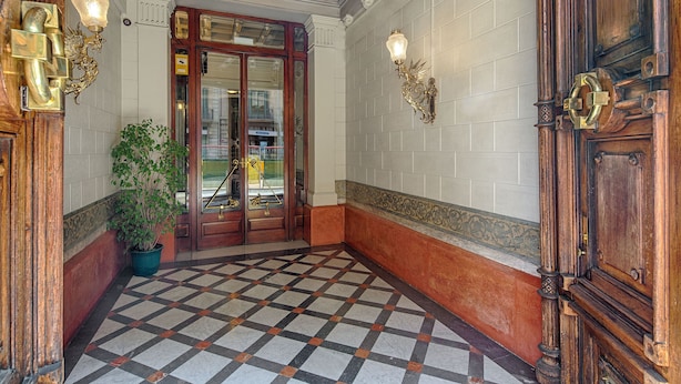 Un hall d’entrée avec un sol à carreaux, des portes en bois et des appliques murales.