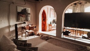 Una sala de estar acogedora con un sofá, un escritorio y una televisión. Hay dos arcos que dan a otra habitación.
