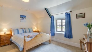 Un dormitorio con una cama de madera, dos mesitas de noche con lámparas, una ventana con cortinas azules y un cuadro en la pared.