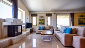 A spacious living room with a fireplace, a sofa set, and a television. - Palladio Luxury Villa with amazing view (Roussospiti)