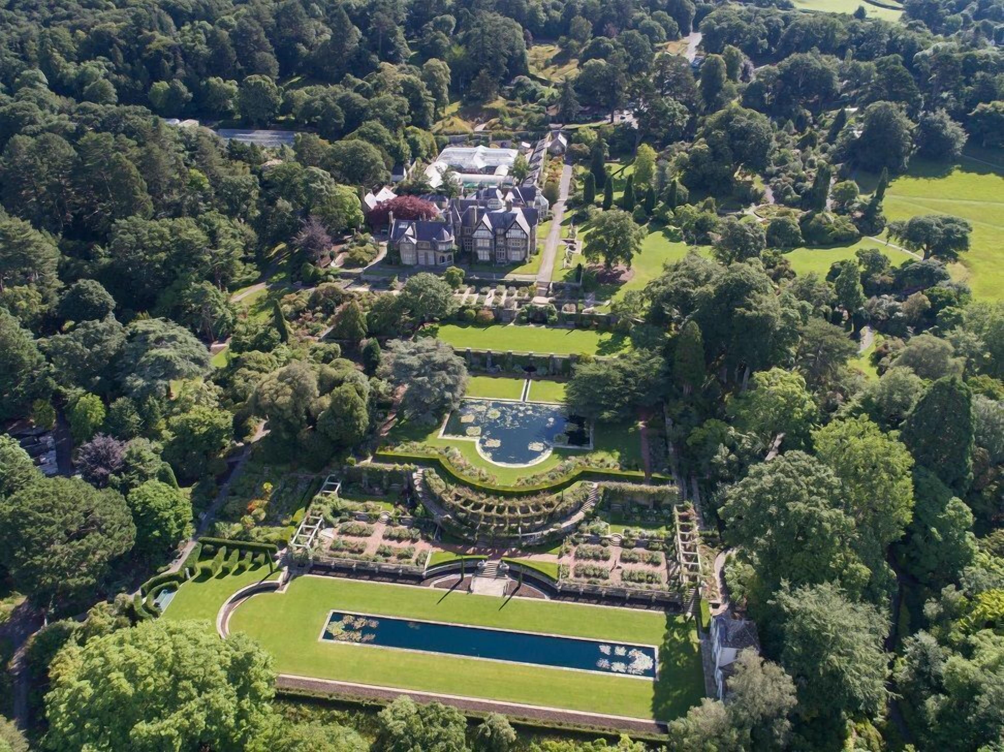 An aerial view of a large estate with a central building surrounded by manicured gardens and a large rectangular pond.