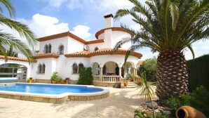 Una villa blanca con piscina, palmeras y un patio de piedra.