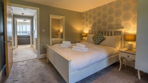 A neatly made bed with towels, a bedside table with a lamp, a mirror, and a patterned wall.