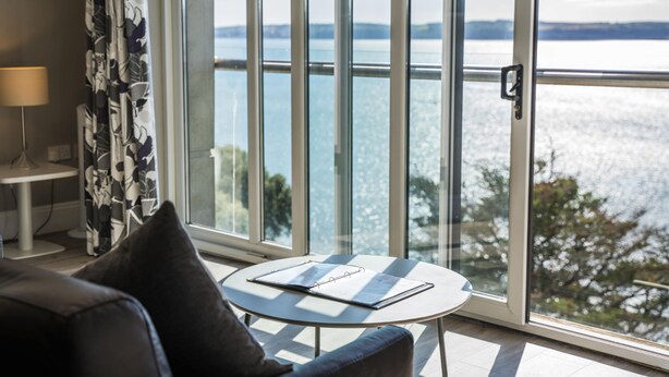 A room with a large window, a round table with a notebook, a lamp, and a sofa.