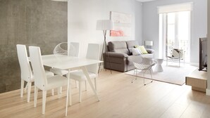 A modern living room with a white dining table and chairs, a grey sofa with cushions, a floor lamp, and a large window with a balcony. - Zabaleta Beach by FeelFree Rentals (Donostia)