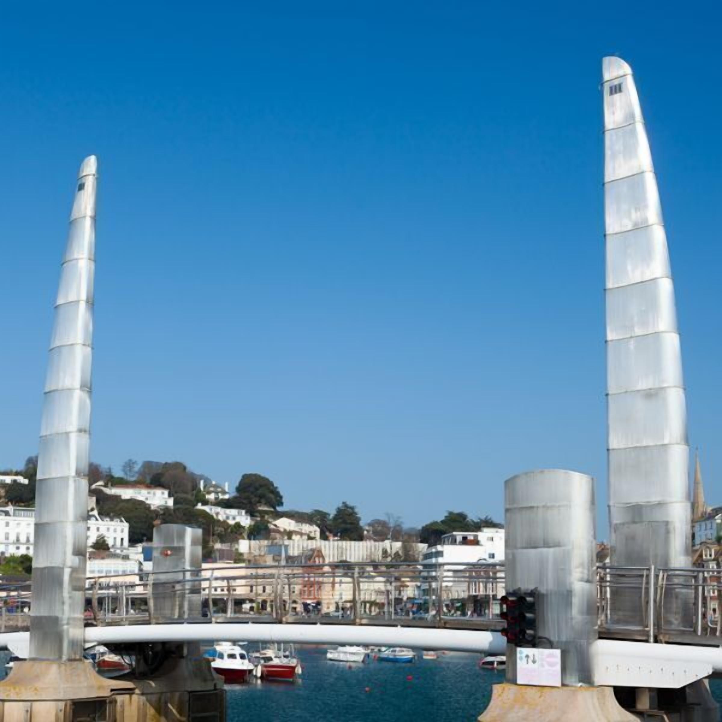 A harbor with two tall, metallic structures, a bridge, and boats.