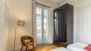 Une pièce comprenant un lit, une chaise, une lampe sur pied et une porte coulissante donnant sur un balcon.