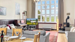 A spacious living room with a fireplace, a television, a piano, and a dining area set for a meal. - The School House, Countisbury (Lynton)