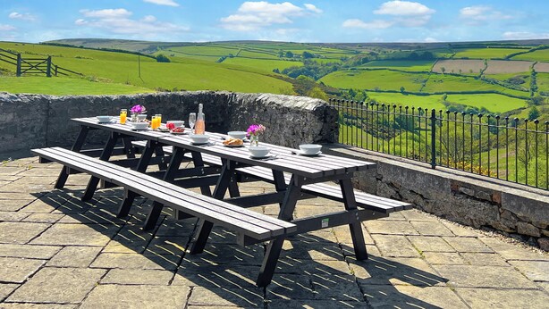 A picnic table set on a stone patio with a scenic view of green fields and a stone wall. - The School House, Countisbury (Lynton)