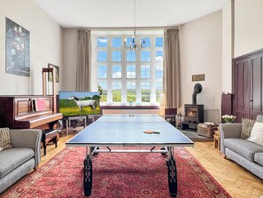 Uma sala de estar com mesa de pingue-pongue, lareira, sofá, televisão e uma janela grande com vista para o campo.