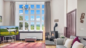 A living room with a large window, a fireplace, a sofa, and a television. - The School House, Countisbury (Lynton)
