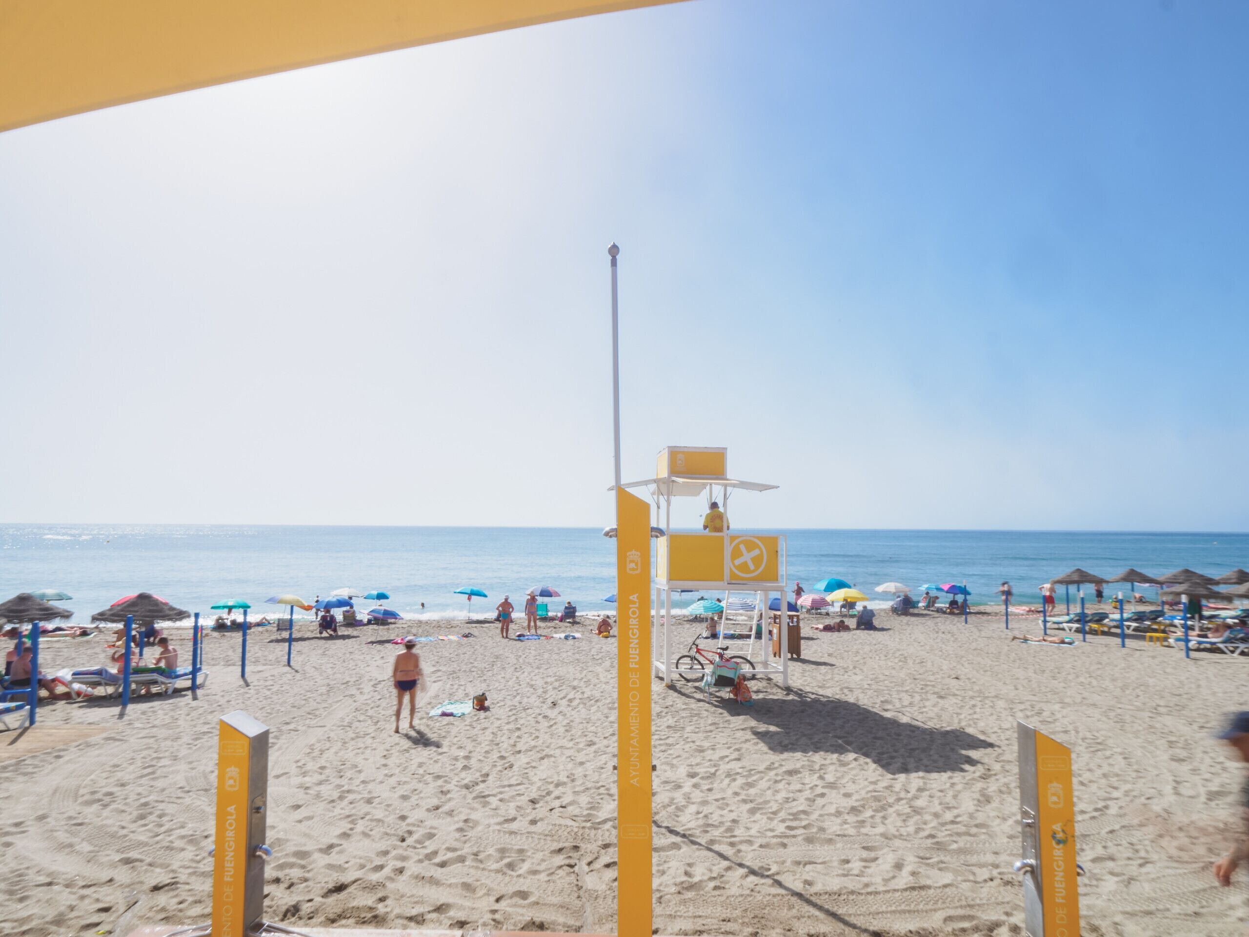 A beach with a lifeguard tower, umbrellas, and beach chairs.