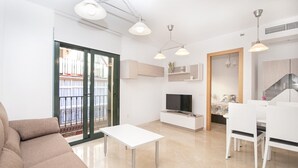 Ein modernes Wohnzimmer mit Sofa, Fernseher, Essbereich mit Stühlen und Küchenzeile mit Herd.