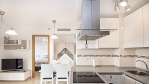 Eine moderne Küche mit weißen Schränken, einem eingebauten Ofen, einer Spülmaschine und einem Essbereich mit Fernseher und Stühlen.