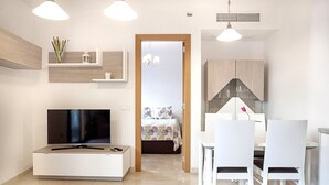 Ein modernes Wohnzimmer mit Flachbildfernseher, weißen Möbeln und Pendelleuchten.
