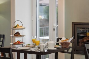 A breakfast setup with a three-tiered serving tray, a teapot, and a basket of bread on a table.