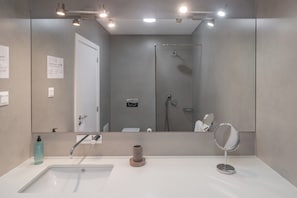 A modern bathroom with a large mirror, two sinks, a shower, and a towel rack.