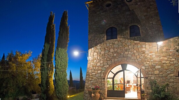 A stone building with a large arched entrance, a small tower, and a well-lit interior. - Historic Stone House Casanova (Cinigiano)