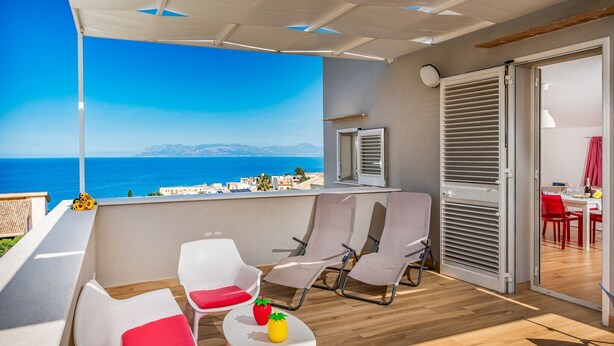 Un balcone con sedie bianche, un tavolino con della frutta e vista sul mare.