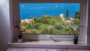 Una finestra con vista su un paesaggio costiero, tra cui vegetazione e un edificio.