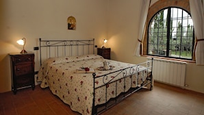 A bedroom with a bed, two bedside tables, a window, and a radiator.