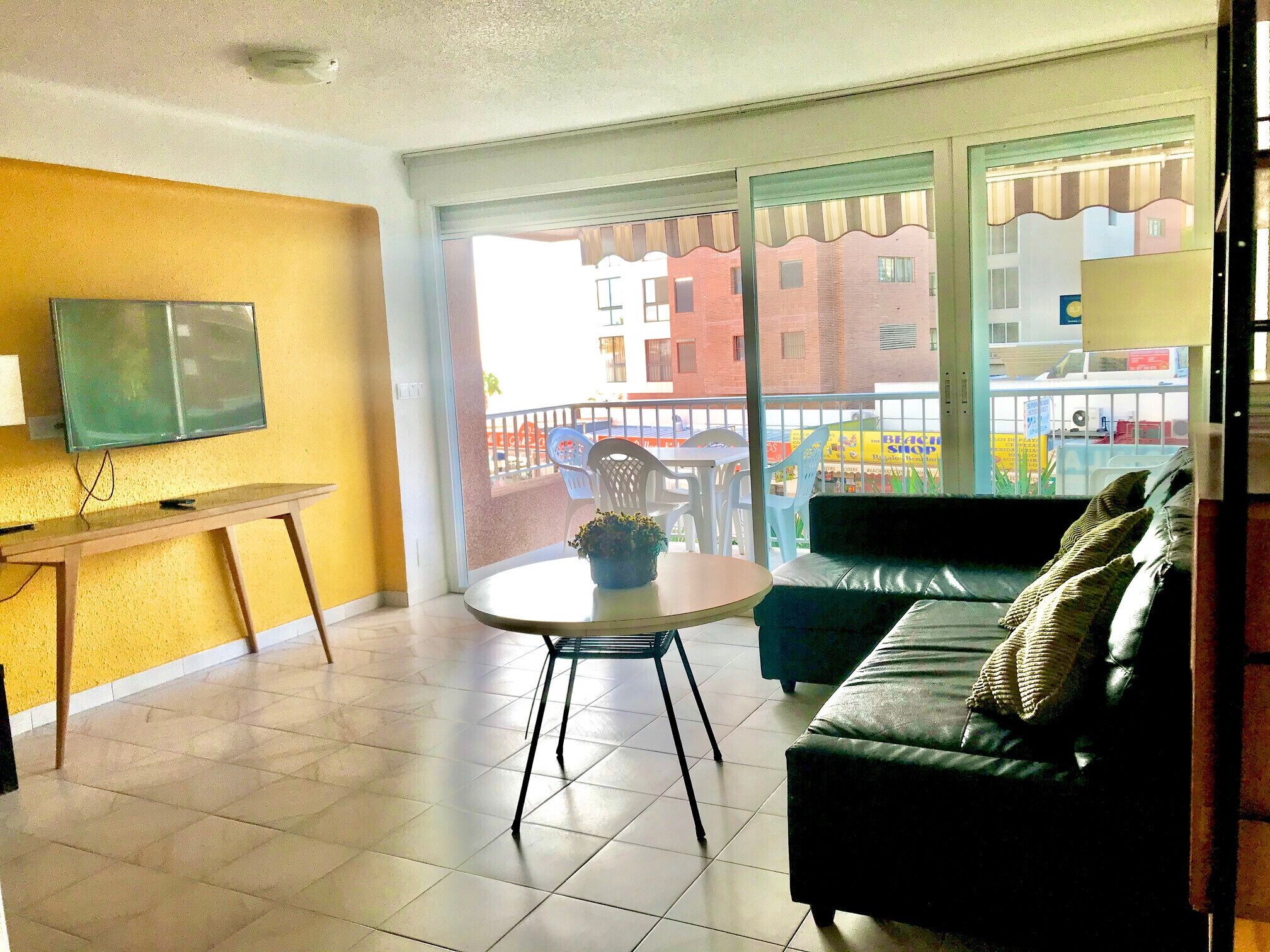 A living room with a sofa, a small table, and a TV mounted on the wall.