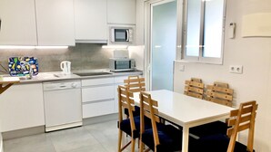 Cozinha compacta com armários brancos, micro-ondas, pia e lava-louças. Há uma mesa de jantar com quatro cadeiras.