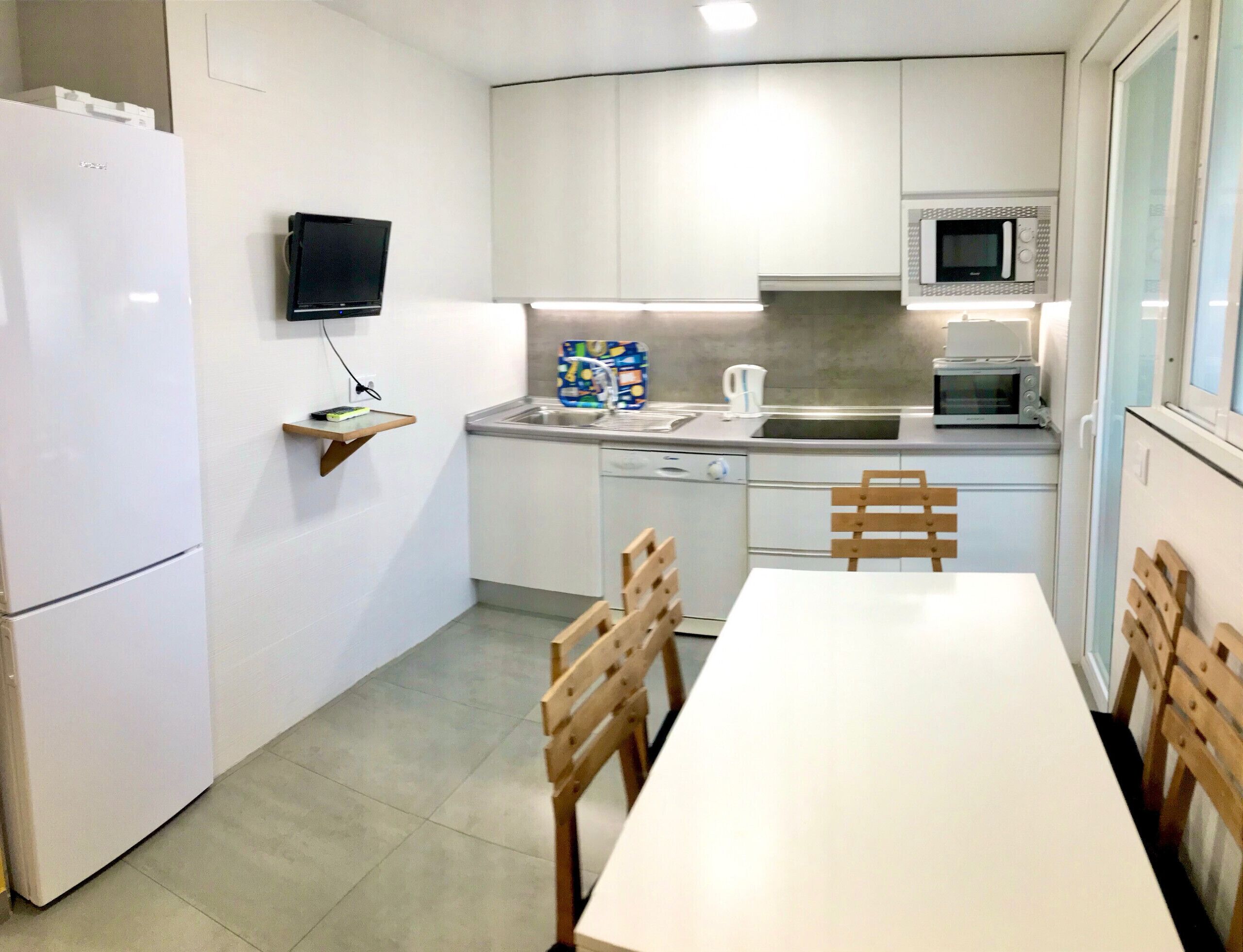 A compact kitchen with white cabinets, a microwave, a dishwasher, and a small table with chairs.