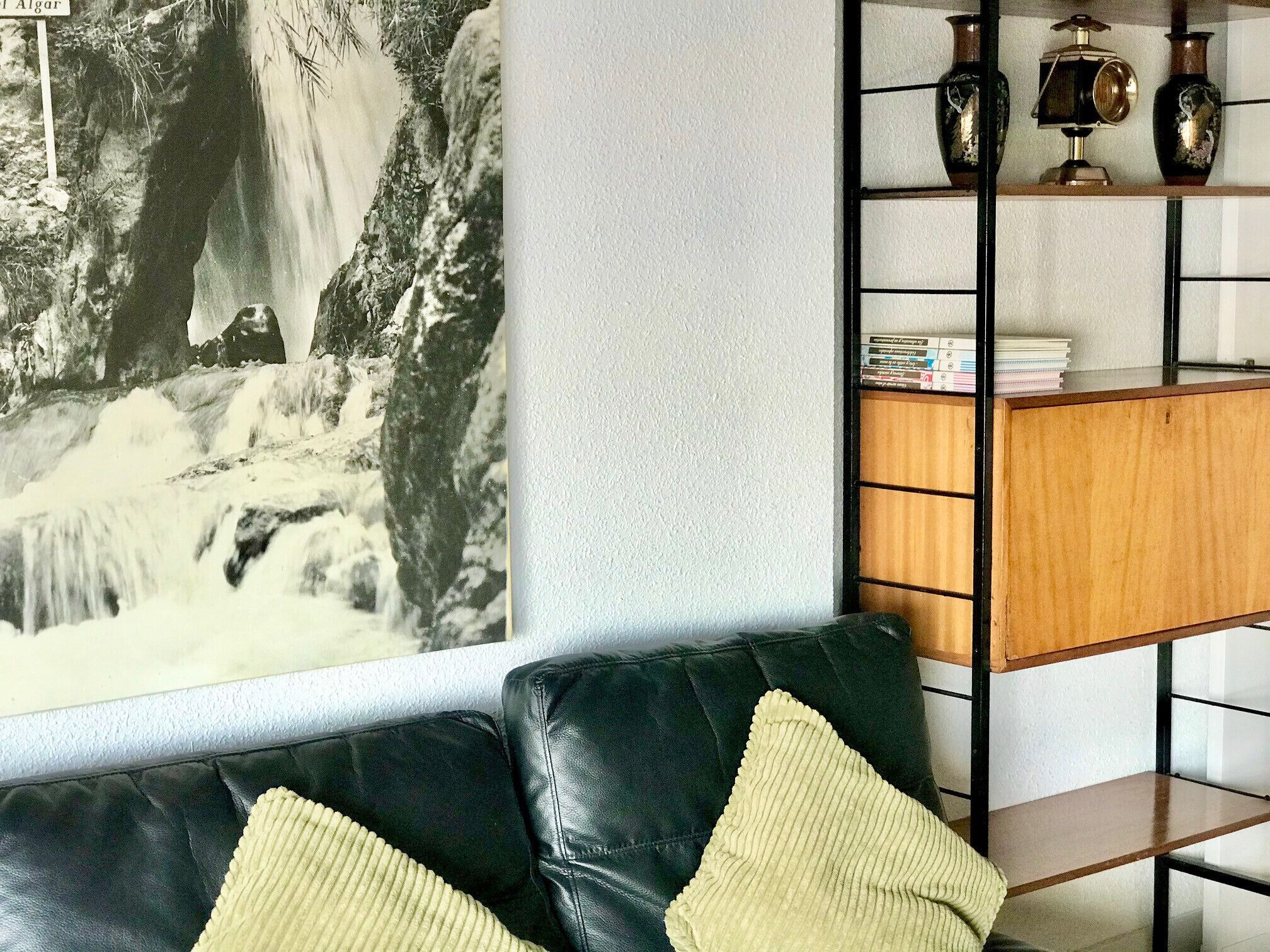A living room with a black leather sofa, a wooden side table, and a bookshelf with decorative items.