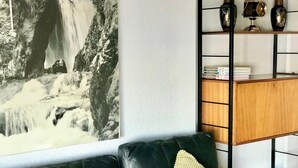 Uma sala de estar com um sofá de couro preto, um aparador de madeira e uma fotografia em preto e branco emoldurada de uma cascata.