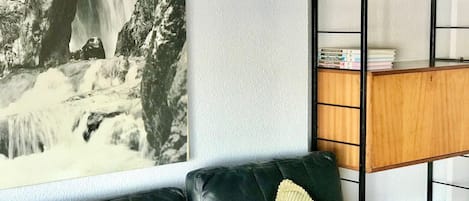 A living room with a black leather sofa, a wooden side table, and a bookshelf with decorative items.