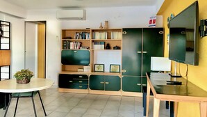 Quarto com uma mesa redonda, estante, televisão e ar condicionado.